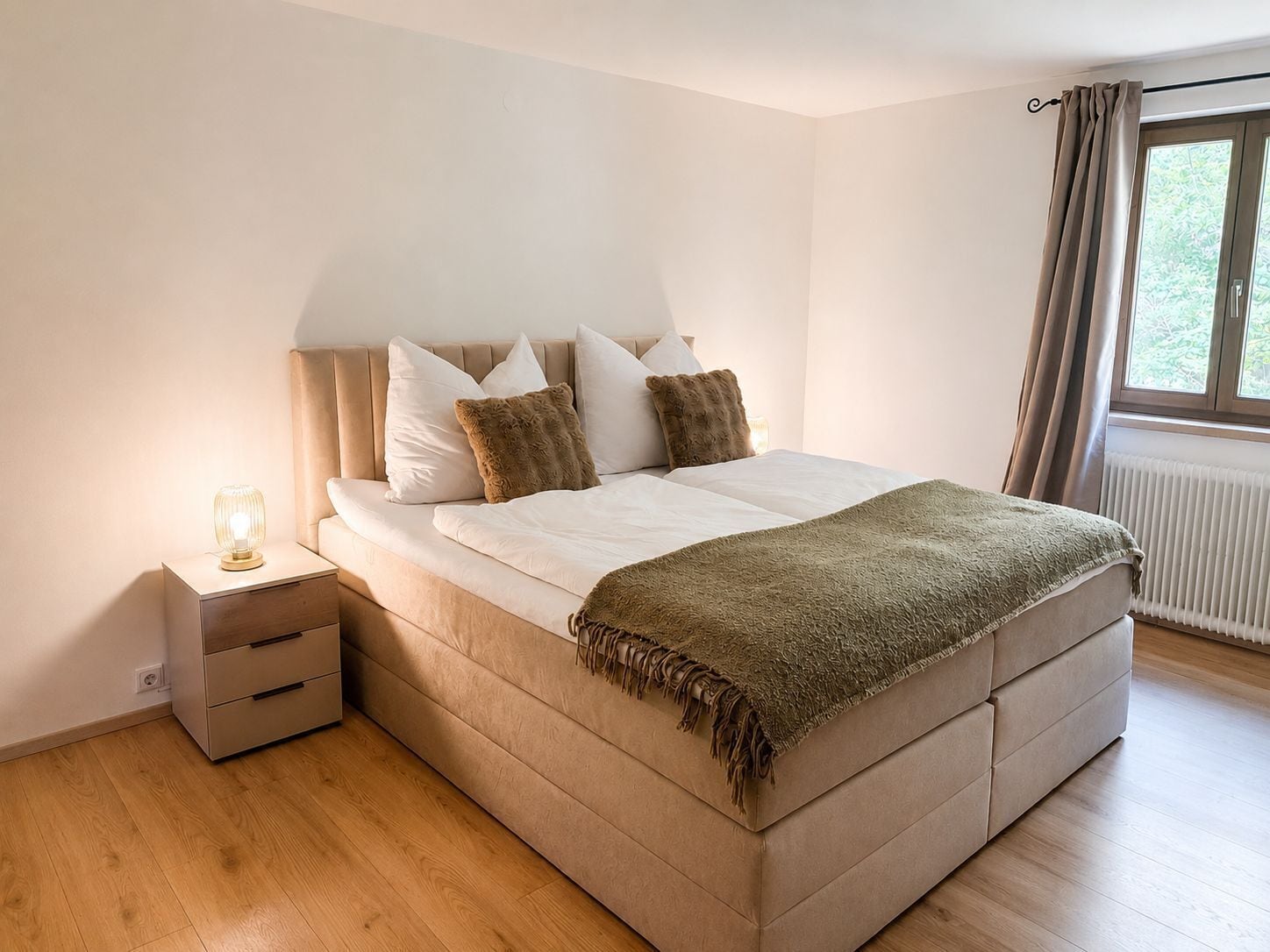 Un dormitorio con cama, mesita de noche y ventana con cortinas.