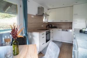 A modern kitchen with white cabinets, a built-in oven, and a window with blue curtains.