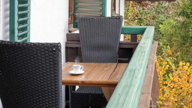 A wooden table with a white cup, a wicker chair, and a bench with green shutters.