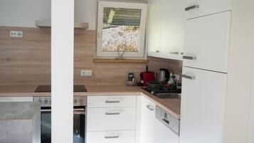 A modern kitchen with white cabinets, a wooden countertop, a built-in oven, a dishwasher, and a window with a view of a garden.