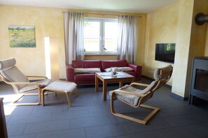 A living room with a red sofa, two wooden chairs, a small table, a TV, and a window with curtains. - with garden and terrace (Glowe)