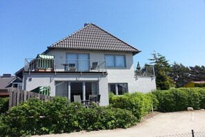 Ein zweistöckiges Haus mit Balkon, einem eingezäunten Garten und blauem Himmel.
