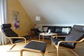 Ein modernes Wohnzimmer mit einer Couch, zwei Sesseln, einem Couchtisch und einer Stehlampe.