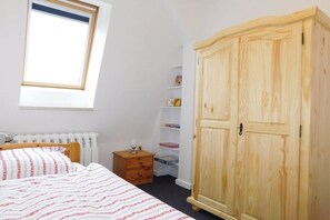 A bedroom with a bed, a wooden wardrobe, a small bedside table, a radiator, and a window with a view. - Holiday apartment with 3 bedrooms (Waldeck)