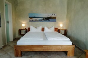 A double bed with a wooden frame, two bedside tables with lamps, and a beach scene painting on the wall. - Sweet child with terrace (Glowe)