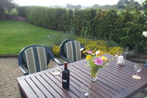 Ein Holztisch mit Stühlen, einer Weinflasche und einem Blumenstrauß.