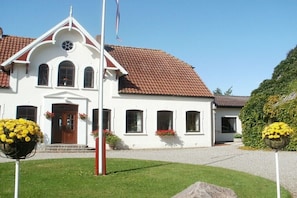 Ein weißes Gebäude mit rotem Ziegeldach, einem zentralen Eingang und Blumenkörben.