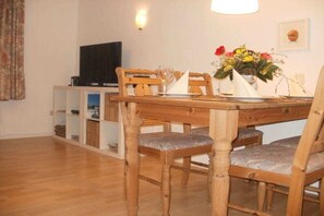 Ein Essbereich mit Holztisch, Stühlen, einem Fernseher und einer Blumenvase.