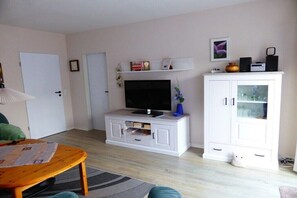 Ein Wohnzimmer mit Fernseher, weißen Schränken, einer Couch und einem Couchtisch.