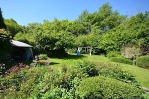 Ein Garten mit Schaukel, Überdachung und verschiedenen Pflanzen.