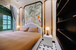 A hotel room with a bed, a nightstand, a bookshelf, a window with curtains, and a decorative wall mural. - Deluxe Indochine 2BR/1BA Panorama view Hoan Kiem Central Hanoi fully equipped (Hà Nội)
