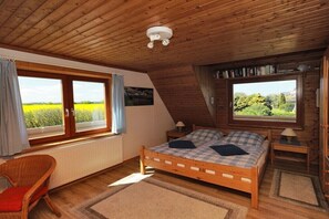 Ein Zimmer mit Holzwandverkleidung, einem Bett, zwei Fenstern, einem Sessel und einer Heizung.