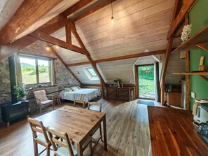 Une chambre mansardée au style rustique, avec un lit, des meubles en bois et une vue sur l’extérieur.