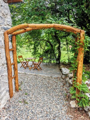 An outdoor seating area with a wooden archway, stone wall, and a gravel path. - Cozy studio on the first floor of a mountain barn (Ercé)