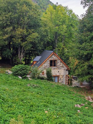 A stone house with a sloped roof surrounded by lush greenery and trees. - Cozy studio on the first floor of a mountain barn (Ercé)
