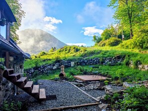 A rustic cabin with a stone exterior, a wooden deck, and a stone wall. - Cosy studio on the first floor of a mountain barn (Ercé)