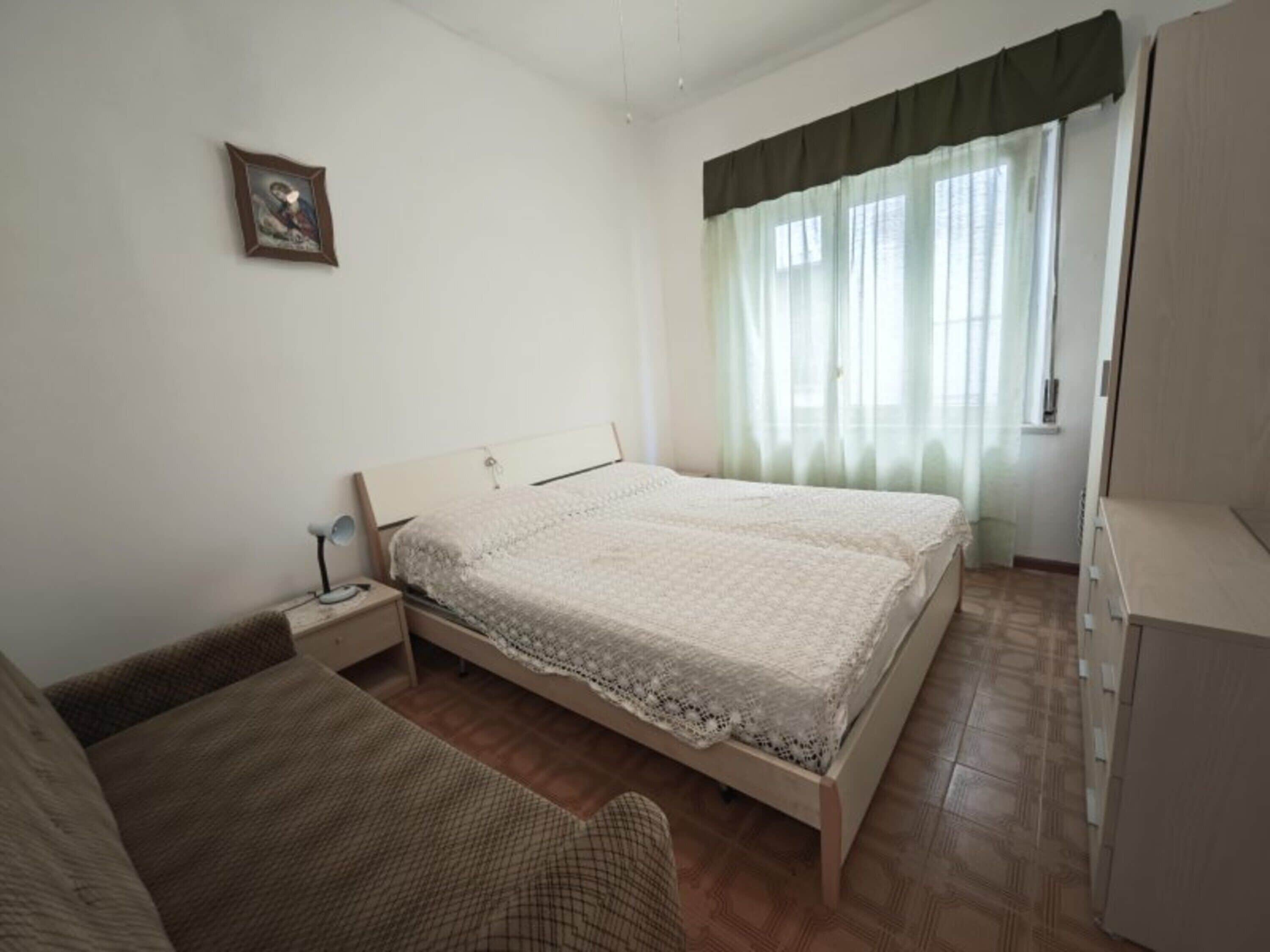 Une chambre à coucher avec un lit, une table de chevet avec une lampe, une armoire et une fenêtre avec des rideaux.