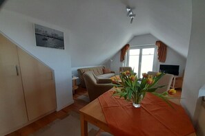 Ein kleiner, gemütlicher Raum mit Esstisch, einer Couch, einem Fernseher und einem Fenster mit Vorhängen.