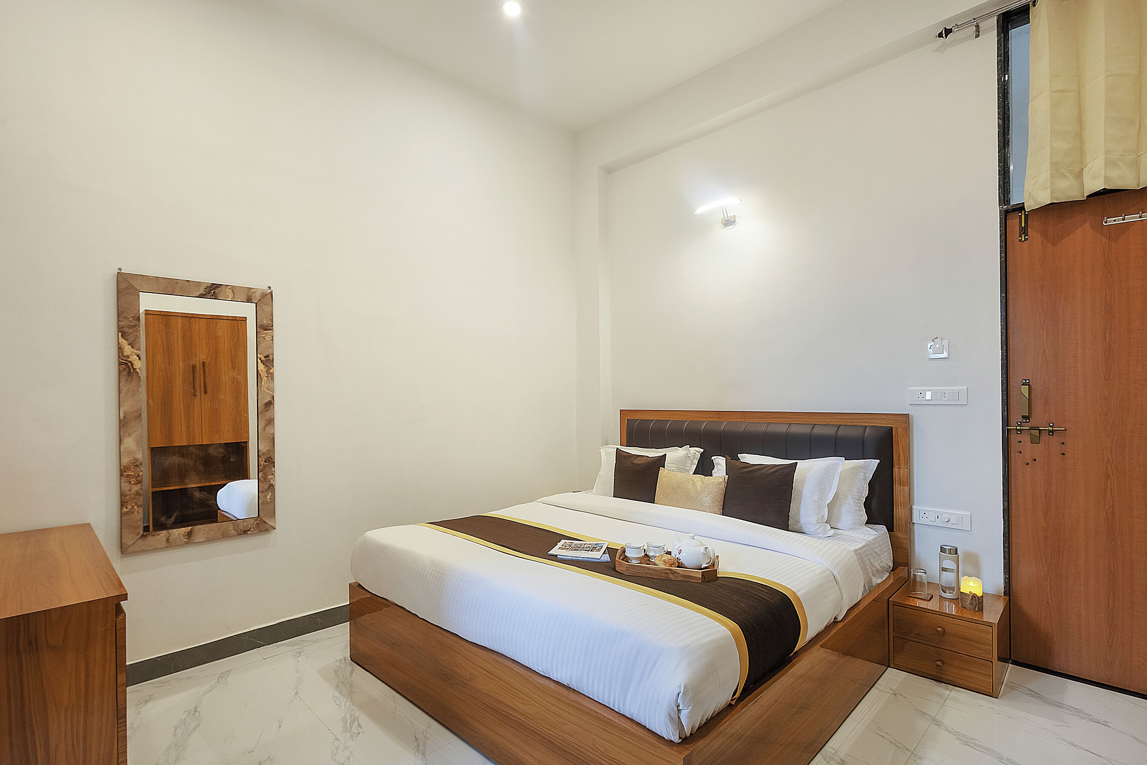 Una camera d'albergo con un letto grande, comodini, una testiera in legno, uno specchio e una porta.