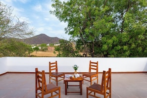 A terrace with four wooden chairs, a small table with a vase and a book, and a view of a mountain and trees. - Hiara Crystal 5BHK Villa with Pool (Udaipur)