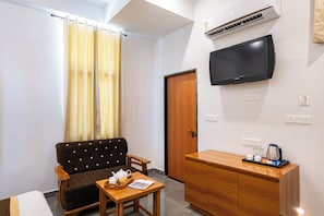A room with a sofa, a small table with a tray, a wooden cabinet, a television mounted on the wall, and a door. - Hiara Crystal 5BHK Villa with Pool (Udaipur)