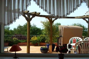 Eine überdachte Terrasse mit Korbmöbeln, Topfpflanzen und Blick auf den Garten.