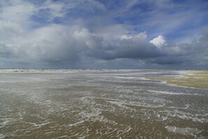 Ein Strand mit Wellen, bewölktem Himmel und einer entfernten Küstenlinie.