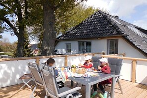 En matplats med ett bord och stolar, ett trädäck och ett hus med ett tak täckt av takpannor.