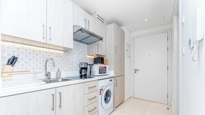 A modern kitchen with a washing machine, microwave, and sink. - Modern studio in Seven Palm, pool and beach (Dubai)