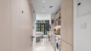 A modern kitchen with a washing machine, a dining area with a table and chairs, and a bedroom with a bed and curtains. - Modern studio in Seven Palm, pool and beach (Dubai)
