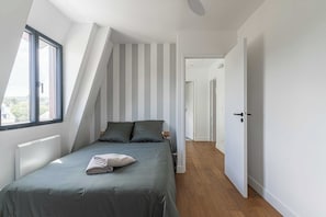 Ein Schlafzimmer mit Schrägwand, einem Bett mit grüner Bettwäsche, einem Heizkörper und einem Fenster.
