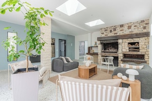 Ein modernes Wohnzimmer mit Kamin aus Stein, einer großen Pflanze und einer gemütlichen Sitzecke.