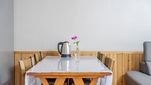 A dining table with a kettle and a vase with a flower, surrounded by wooden chairs.