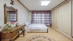 A bedroom with a wooden dresser, a bed with floral bedding, a mirror, and striped curtains.