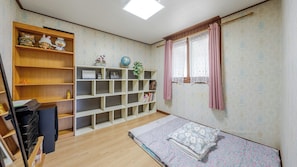 A room with a wooden floor, a bed with floral bedding, a bookshelf, and a window with curtains.