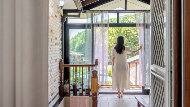 A woman in a white dress standing on a balcony with a view of greenery and buildings. - Jangmi Pension, Daebudo (Incheon)