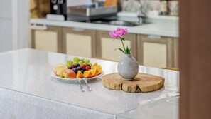 Uma bancada de cozinha com um prato de frutas, um vaso com uma flor e uma tábua de corte de madeira.