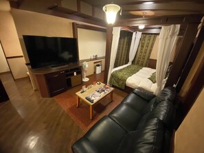 Camera d'albergo con TV, divano, letto a baldacchino, un piccolo tavolino e una ventola.