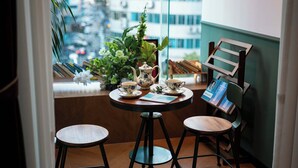 A small round table with a teapot and cups, two stools, a potted plant, and a bookshelf with books and a framed picture. - Xigaodi Art Homestay Hotel  (Guiyang)