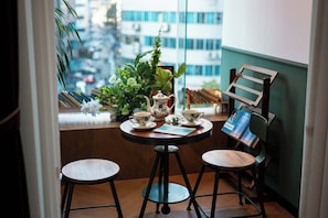A small round table with a teapot and cups, two stools, a potted plant, and a bookshelf with books and a framed picture. - Xigaodi Art Homestay Hotel  (Guiyang)