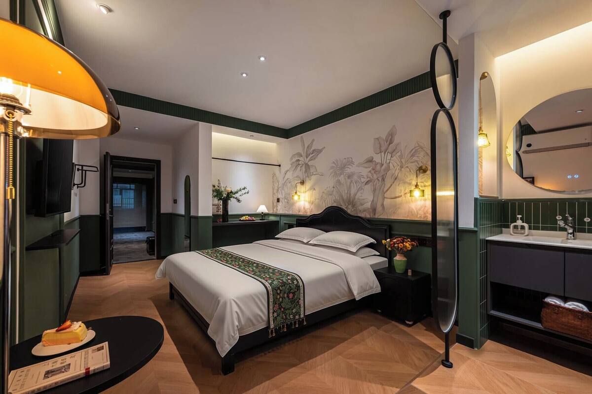 A hotel room with a bed, bedside table, lamp, and a view of the hallway.