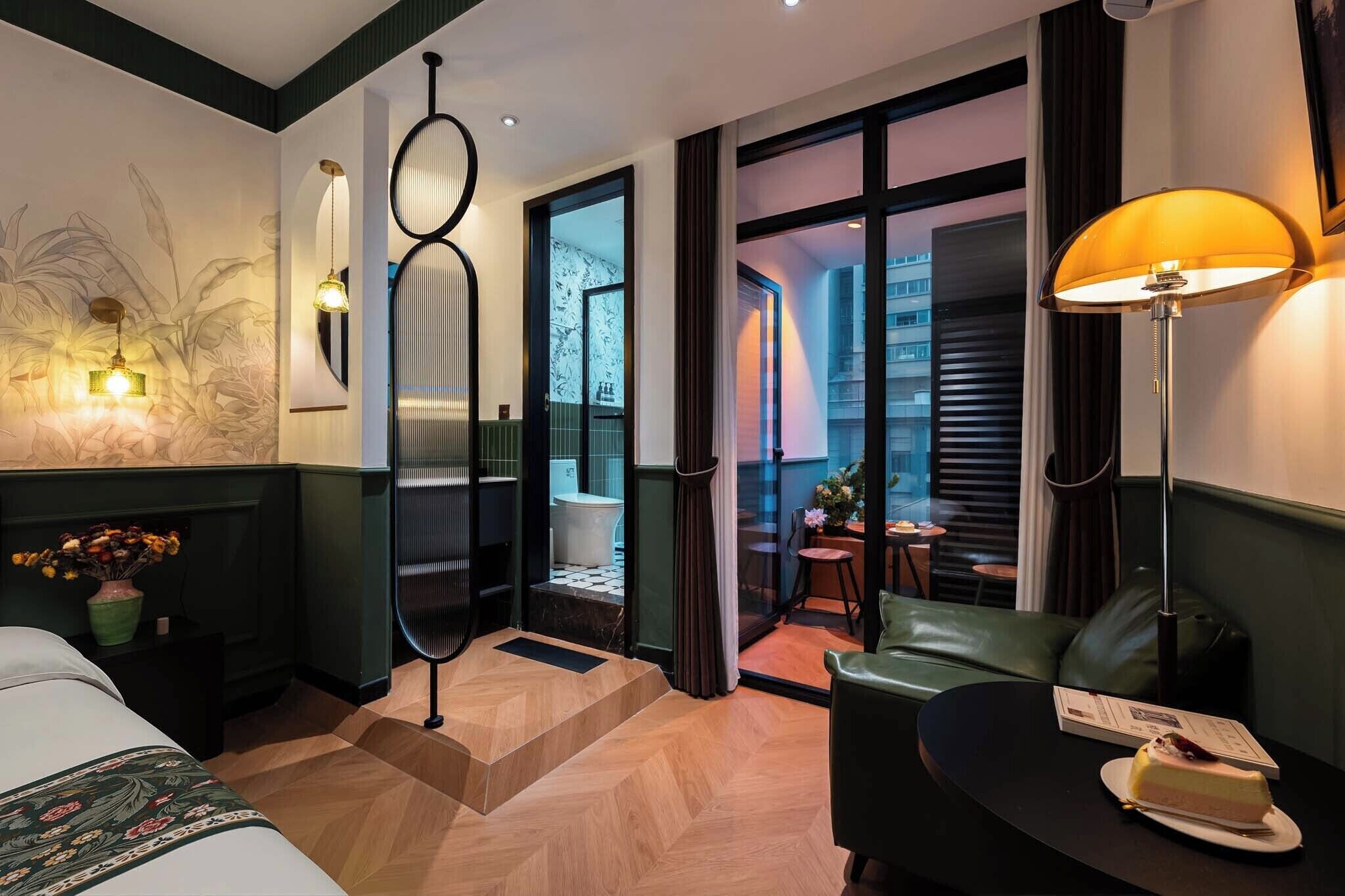 Une chambre d’hôtel moderne avec un lit, un coin salon, une table à manger avec un gâteau, et une vue à travers une porte vitrée.