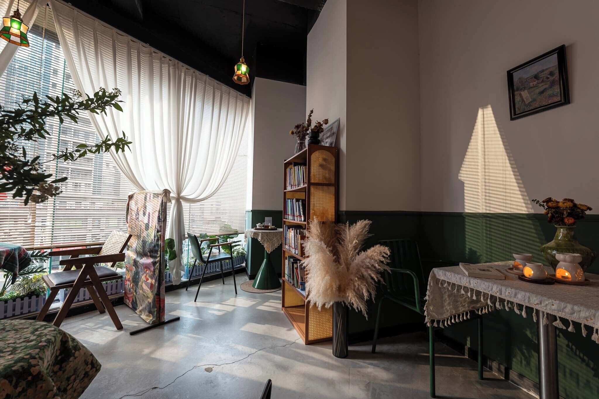 A room with a large window, a bookshelf, a table with candles, and a chair.