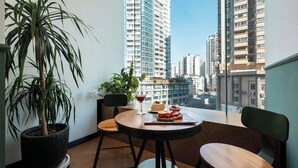 A balcony with a potted plant, a table with a dessert and drink, and a view of high-rise buildings. - Xigaodi Art Homestay Hotel  (Guiyang)