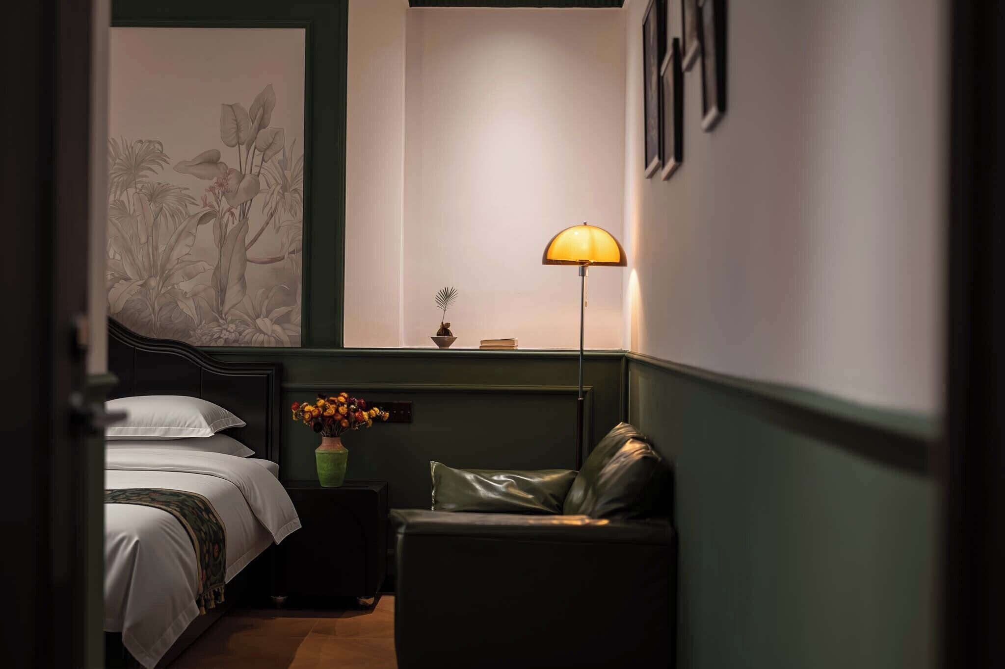 A bedroom with a bed, a desk, a chair, a lamp, and a wall with a plant illustration.
