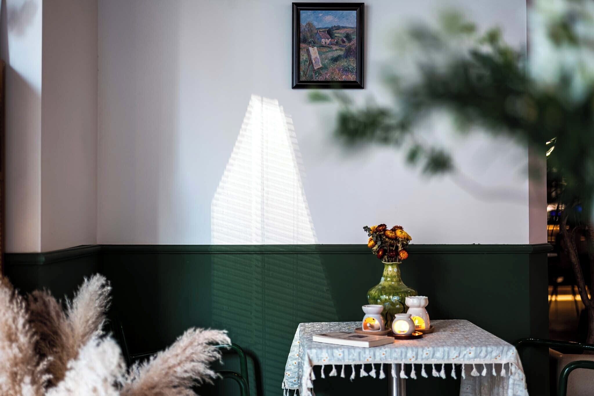 A table with a vase of flowers, a candle, and a small clock, set against a wall with a framed picture.
