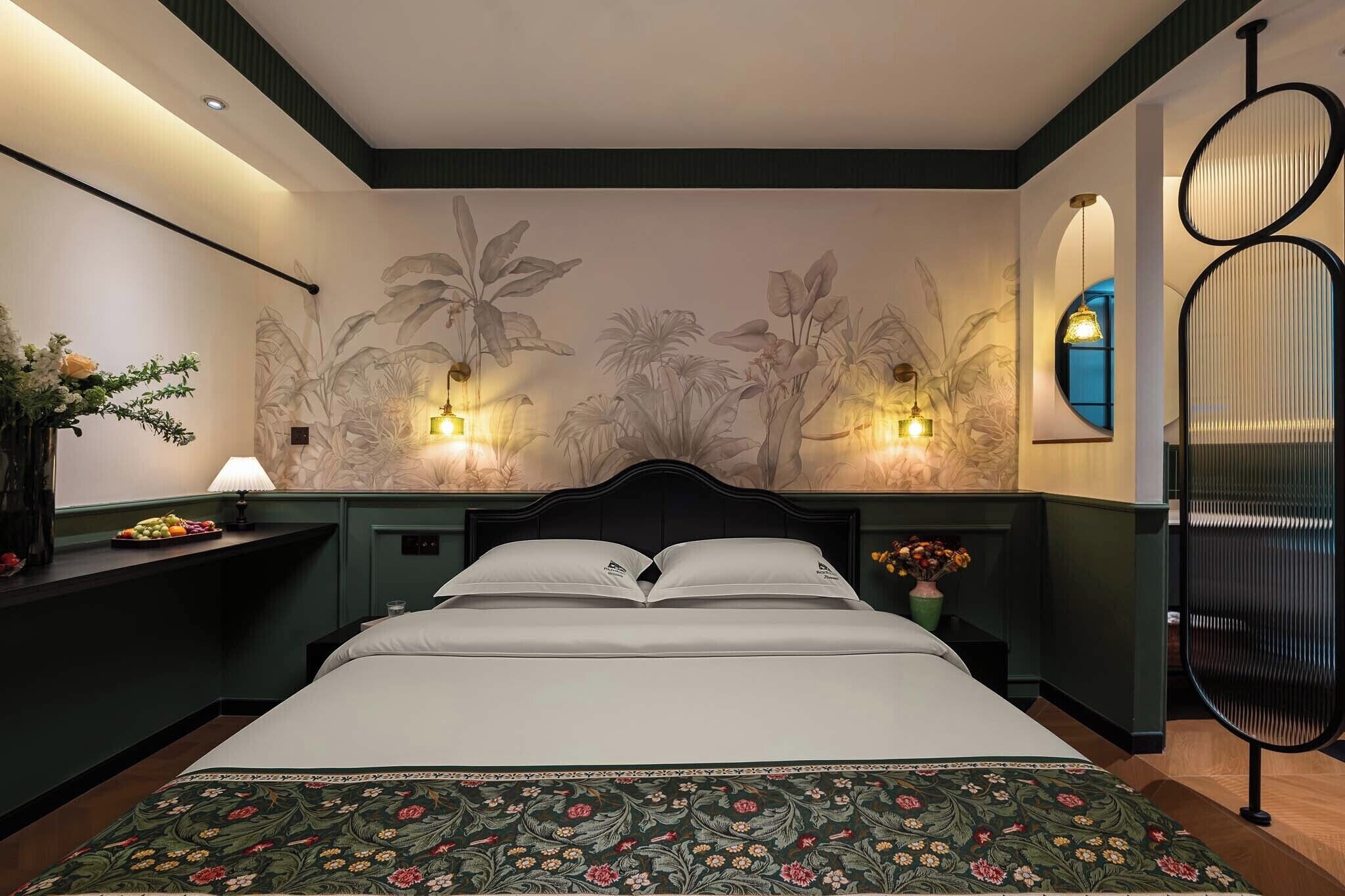 Una habitació d'hotel amb un llit, una tauleta de nit, una làmpada de paret i un mural decoratiu.