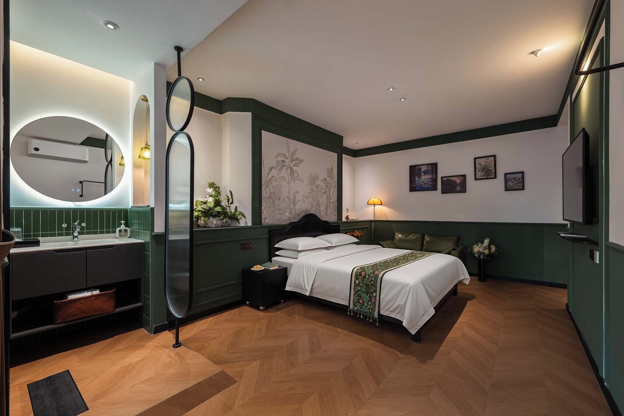 Ein modernes Hotelzimmer mit einem Bett, einem runden Spiegel, einem Schminktisch mit Waschbecken und einem großen Wandbild.