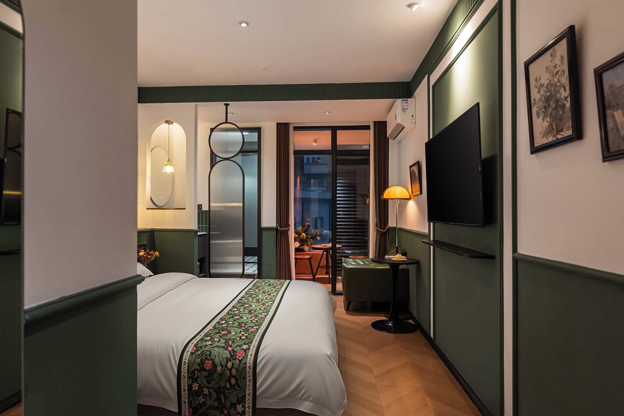 A hotel room with a bed, a TV, a desk, and a view through a door.