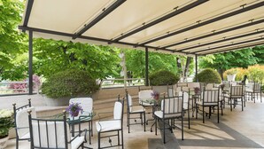 An outdoor patio with a covered seating area, including tables and chairs, surrounded by greenery and potted plants. - Hotel Miralaghi Family & Sport (Chianciano Terme)